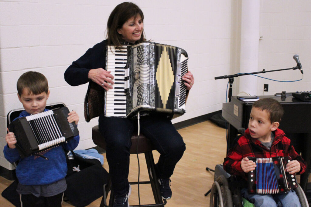 Judy Doyle is flanked by WLES kindergartners, from left, Holden Fecat and Chase Huggins while playing “The Chicken Dance” song on their accordions.